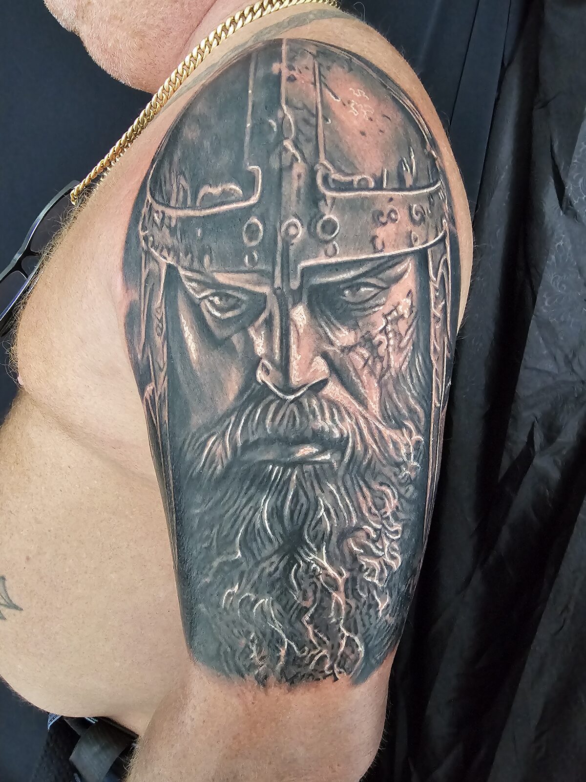 Black-and-grey Norse warrior portrait tattoo on the upper arm by Guy Abergel