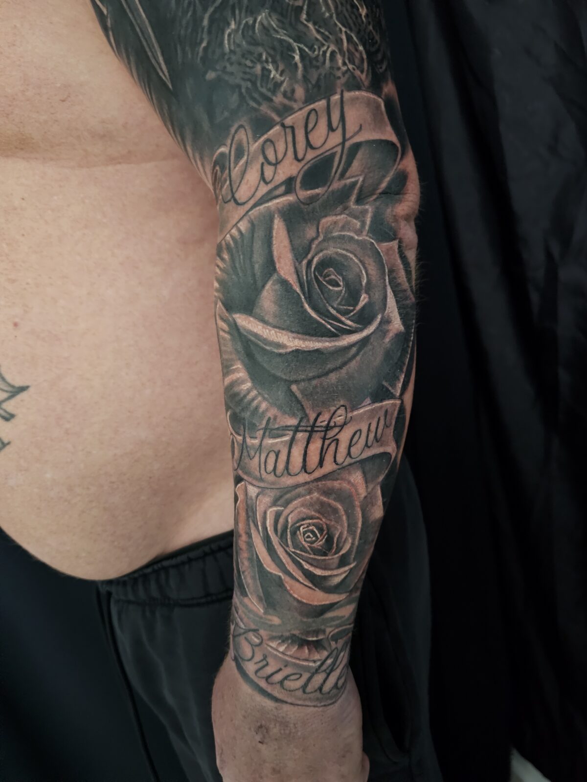 Black-and-grey forearm tattoo with roses and lettering by Guy Abergel